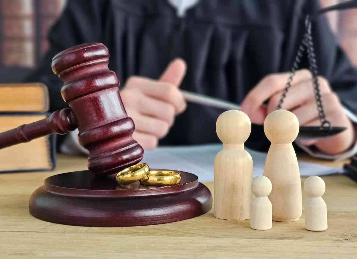 A gavel, small wooden figurines of parents and children, and a judge on a courtroom table with scales of justice. Family law, court, divorce, child custody.