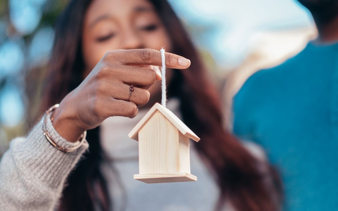 close-up of a woman holding a wooden house symbolizing real estate or homeownership
