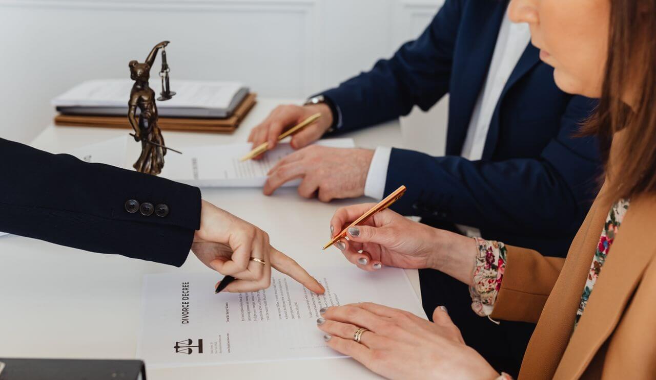 hands signing a divorce decree, with a justice statue nearby, symbolizing legal proceedings