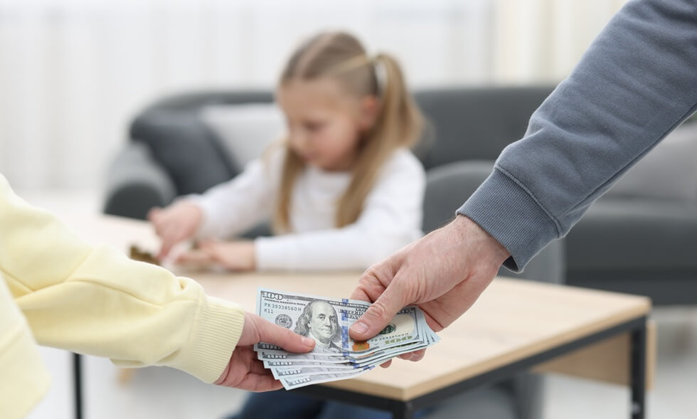 man giving money to ex-wife while his sad daughter counting coins at table indoors, selective focus
